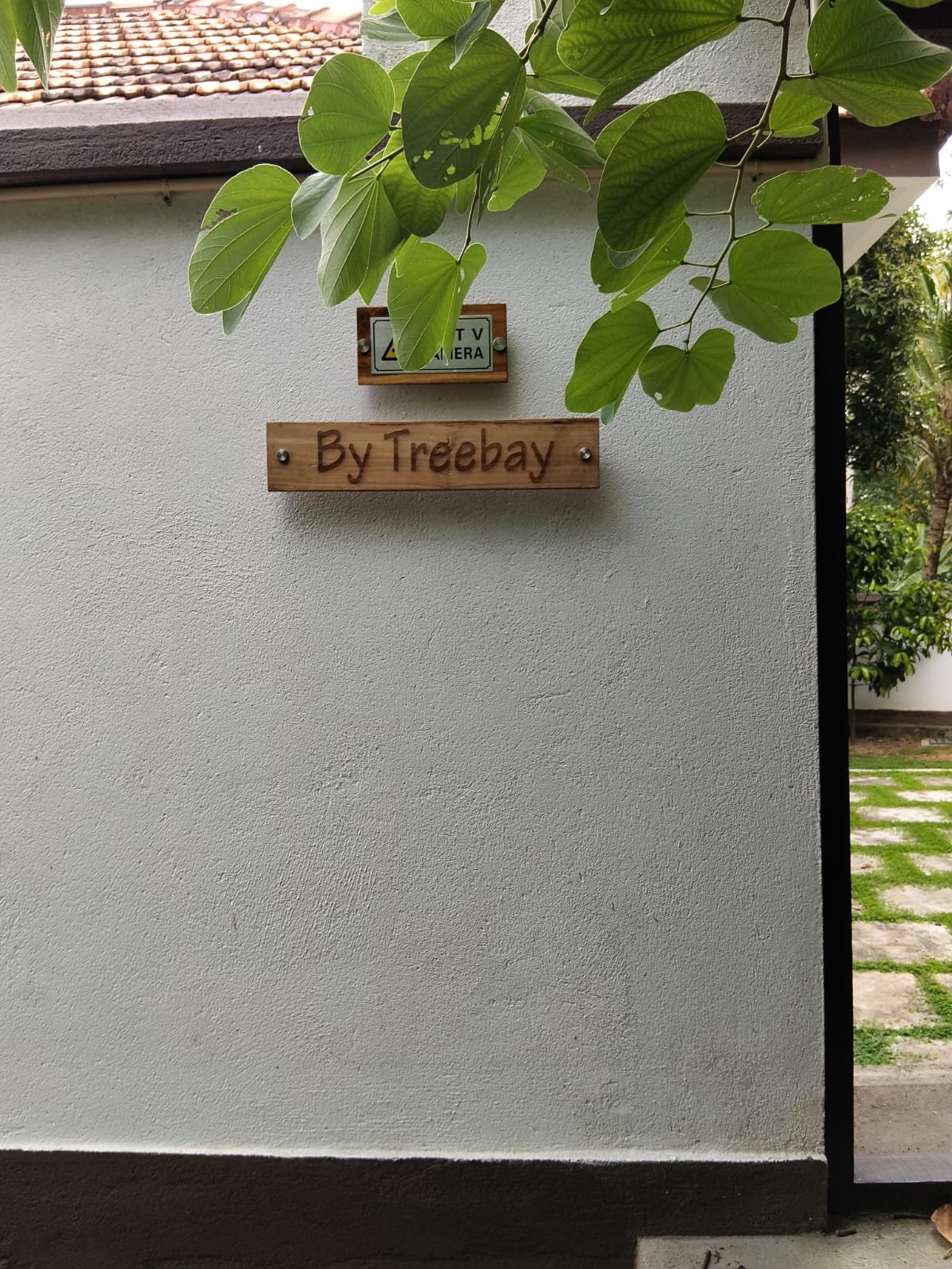 Wooden By Treebay sign on the entrance wall beneath green leaves